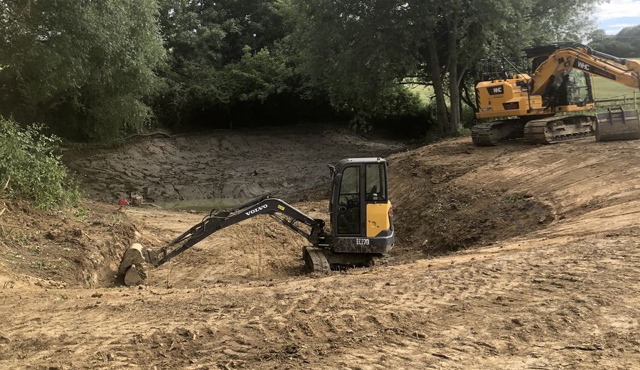 Excavators forming a pond and reshaping ground beside woodland